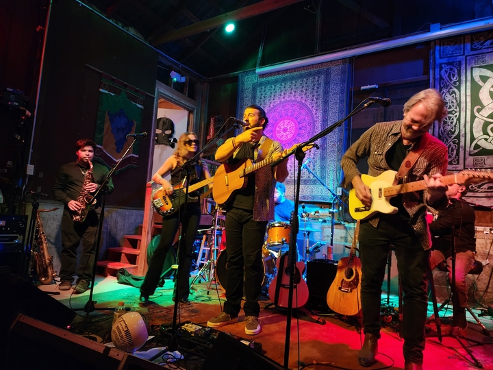 Alex Lucero singing with his band on stage under colored lights